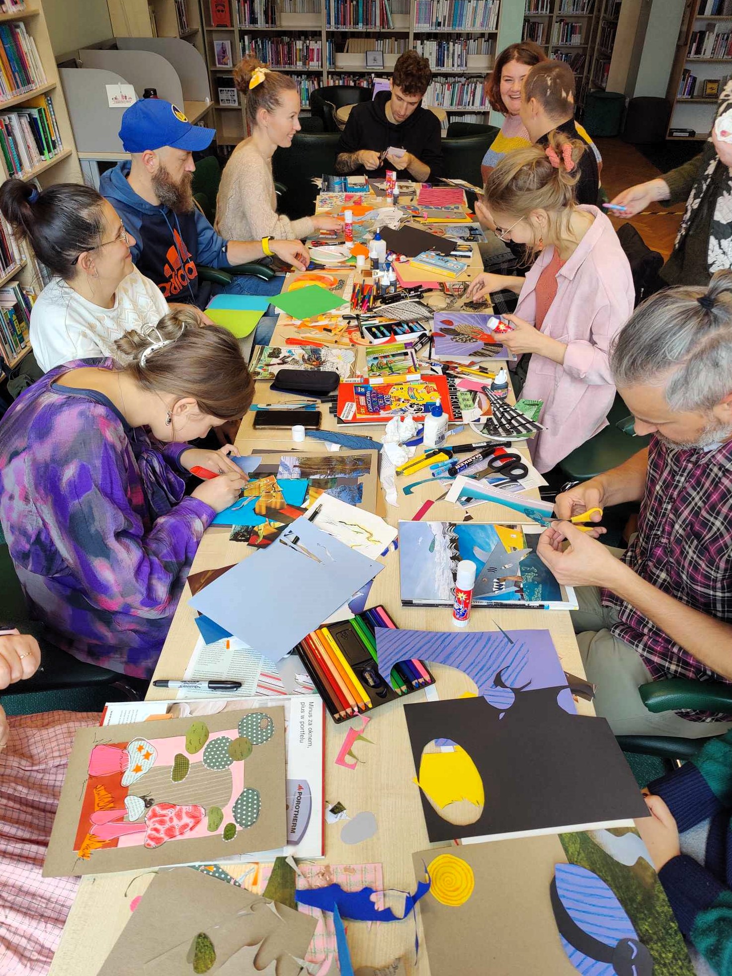 grupa dorosłych ludzi przy stole robi prace plastyczne. 